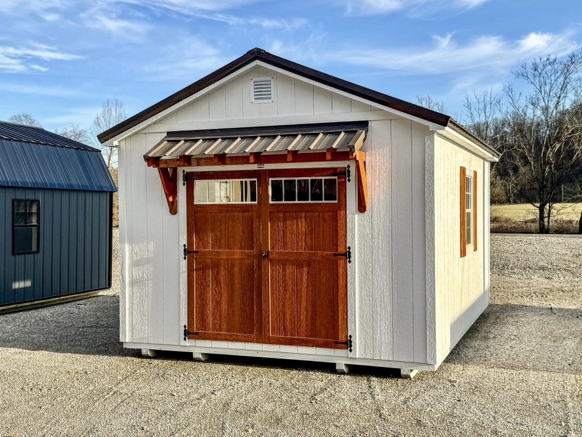 White shed with stained wood double doors, a glass transom window, and a wood bracket awning over the entrance