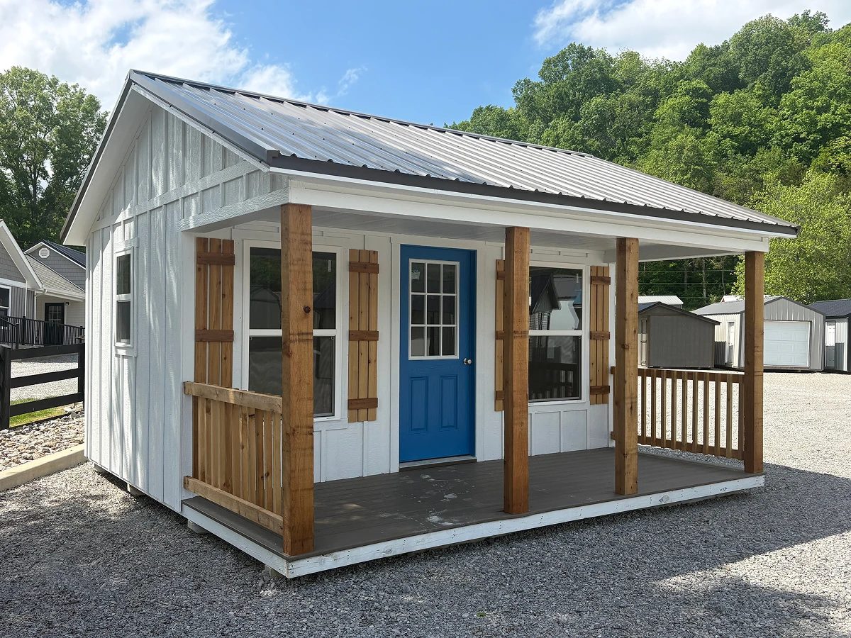 White shed with a covered front porch, wood support posts, a blue door, and wood shutters
