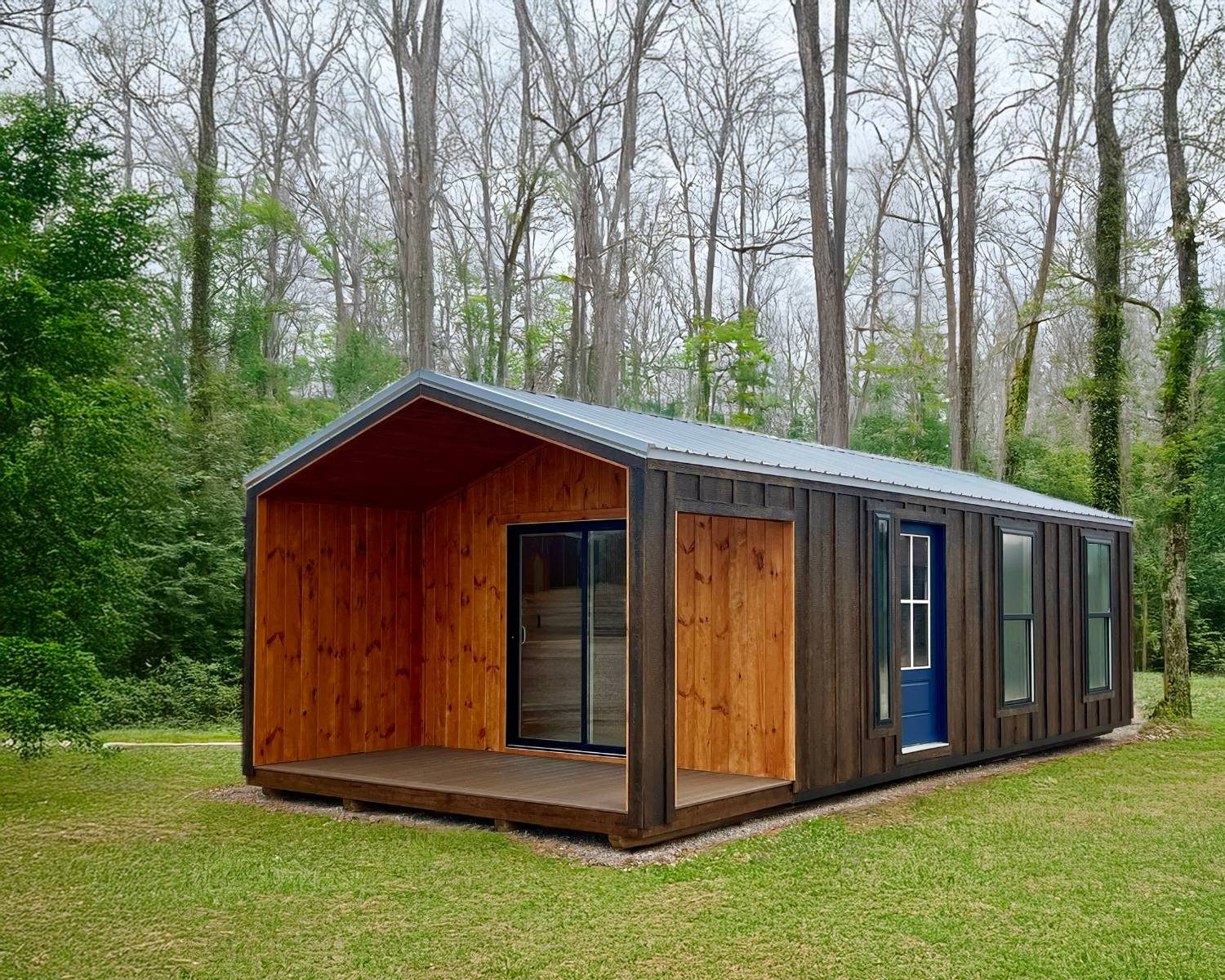 Dark-stained tiny home with an open covered porch, a sliding glass door, and an A-frame gable roof in a wooded setting