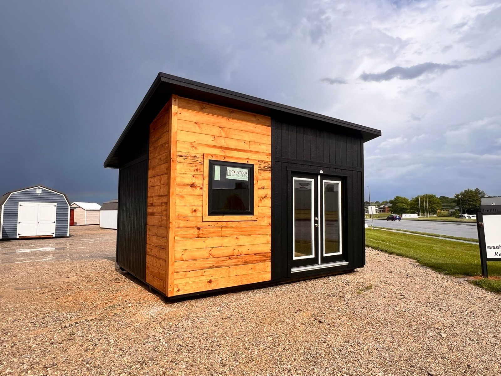 Modern shed-roof tiny home with half natural wood and half black siding, and black double doors