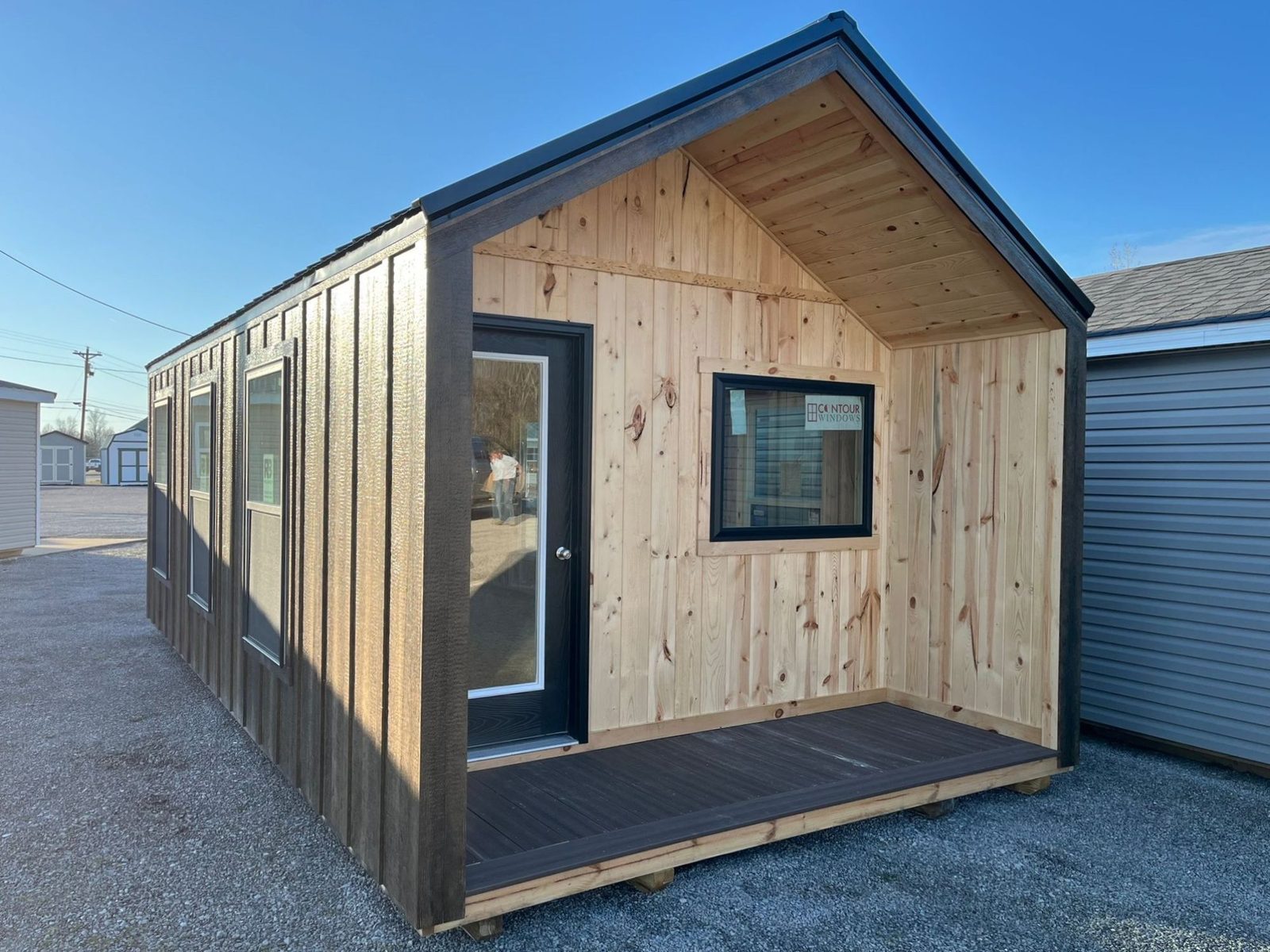 Unstained pine tiny home shell with a small covered porch, a glass door, and a single window