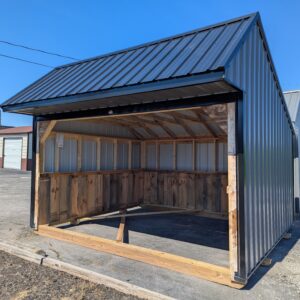 Open-front blue metal shed under construction with corrugated walls and a wooden frame, set against a clear blue sky.