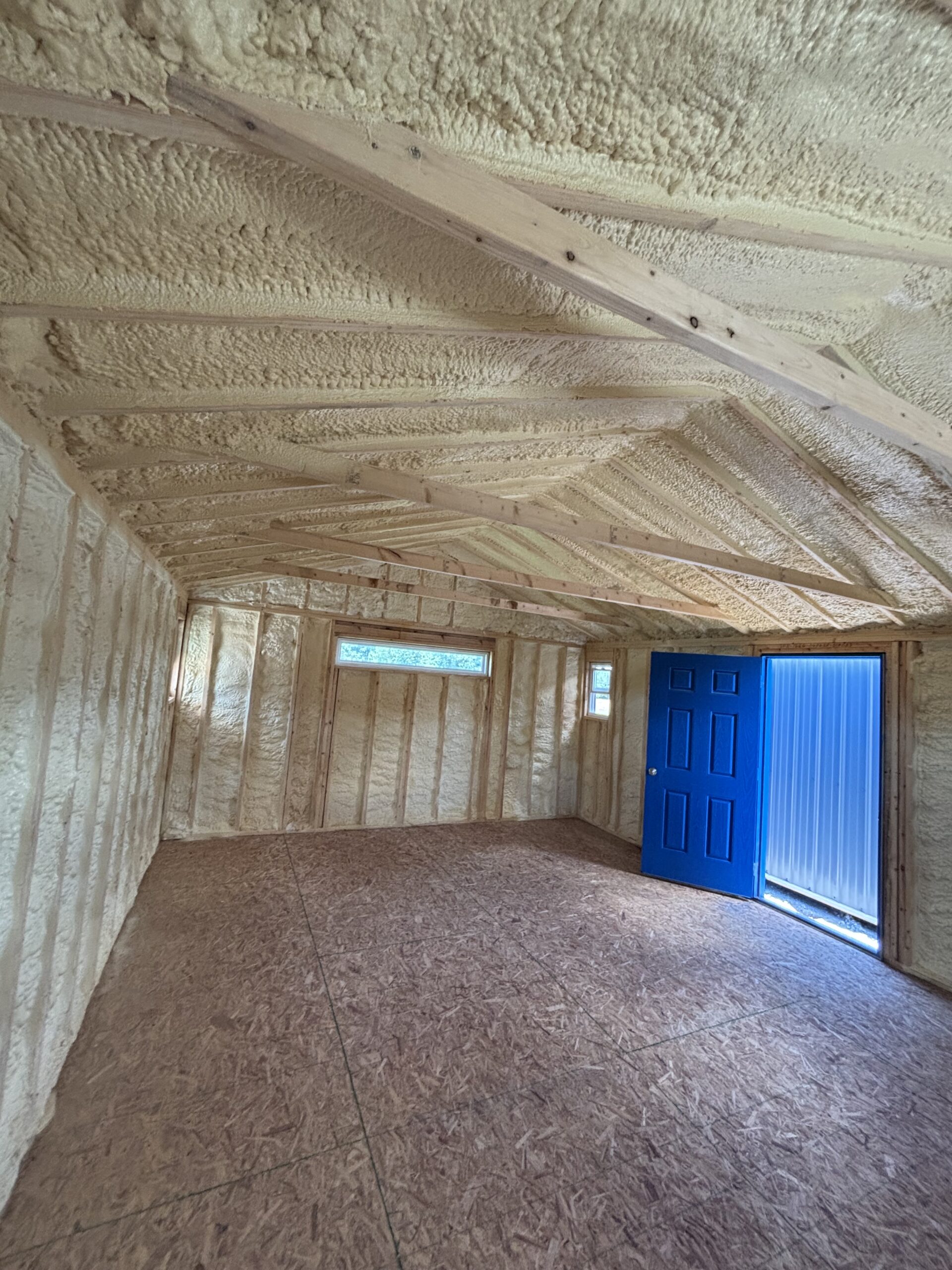 Unfinished room with spray foam insulation on walls and ceiling, exposed wooden framing and a bright blue door.