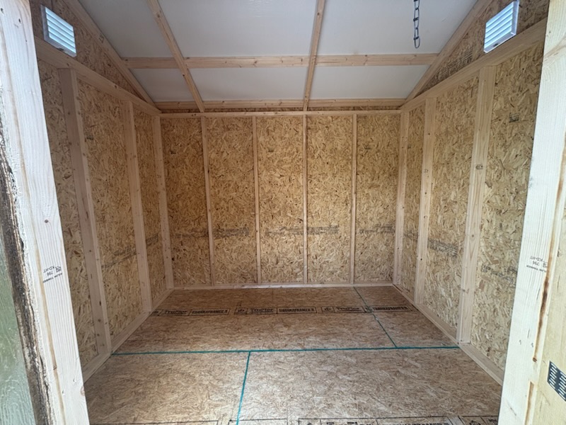 Interior of an unfinished wooden shed with OSB walls, exposed studs, and ventilation openings near the ceiling