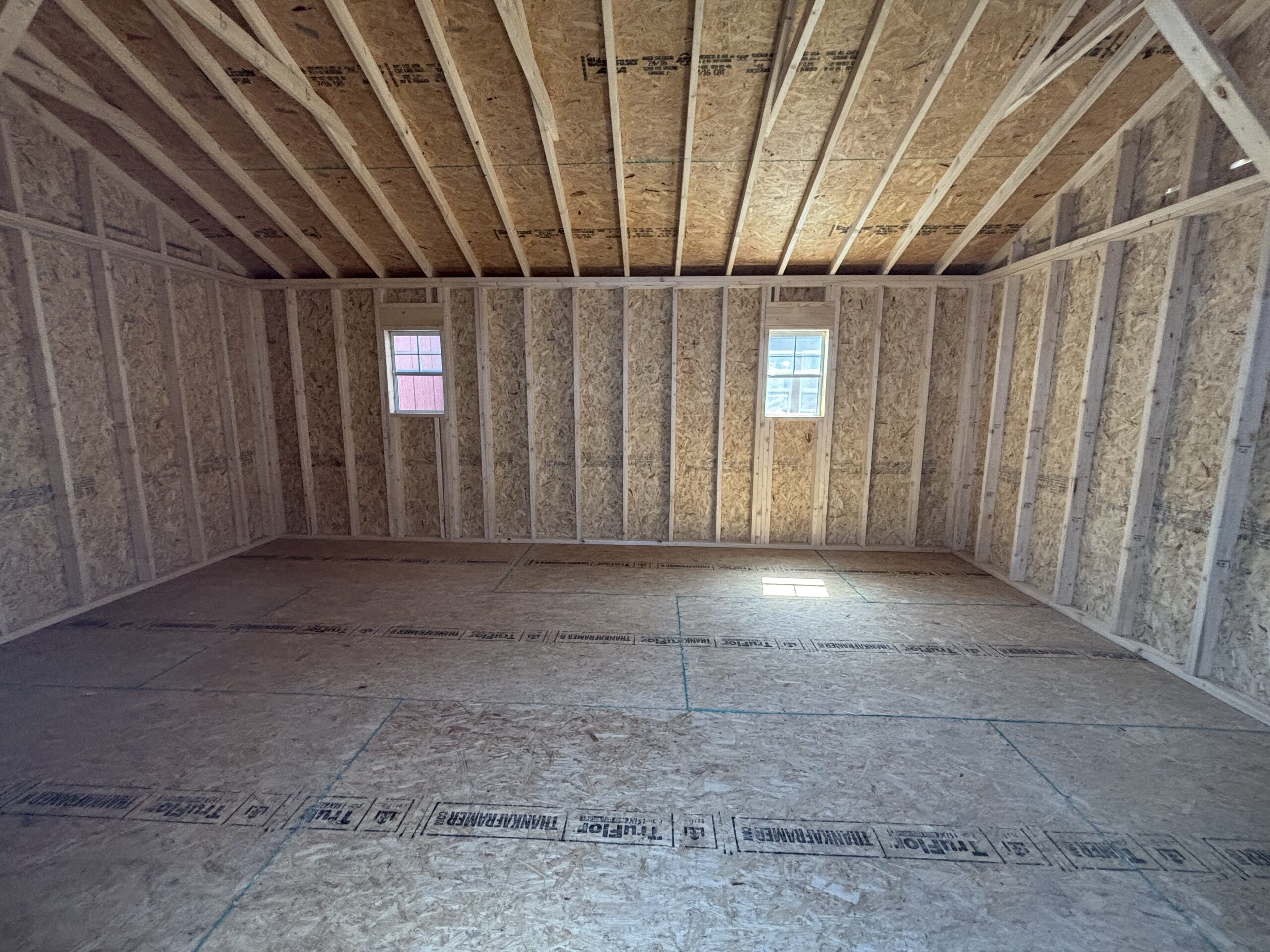 Unfinished attic with exposed wooden framing and two small windows.