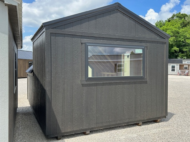 Dark gray wooden shed with a sloped roof and a single rectangular window, sitting on gravel.