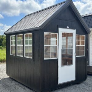Small dark blue wooden cabin with a steep metal roof and large front windows under a partly cloudy sky