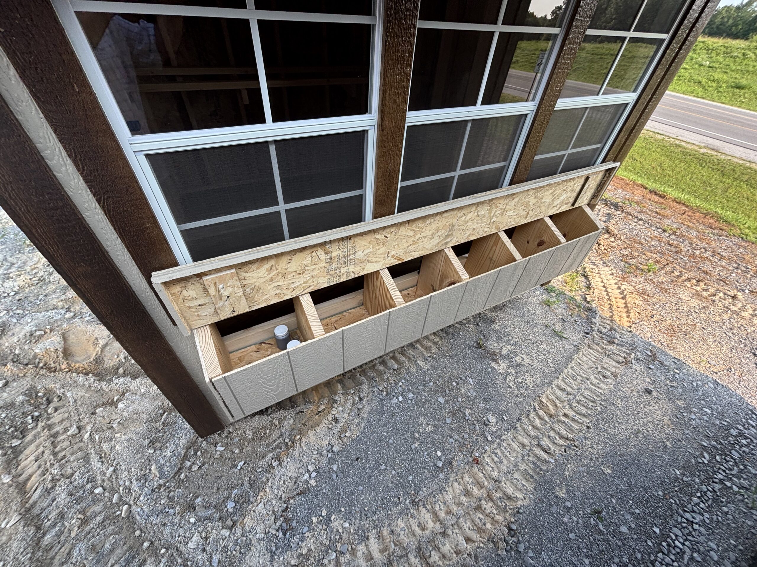 Partial view of a building under construction with large window panes and exposed framing on a gravel site