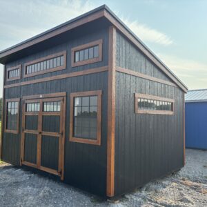 Black barn-style building with brown wooden trim and large rectangular windows on a gravel lot.