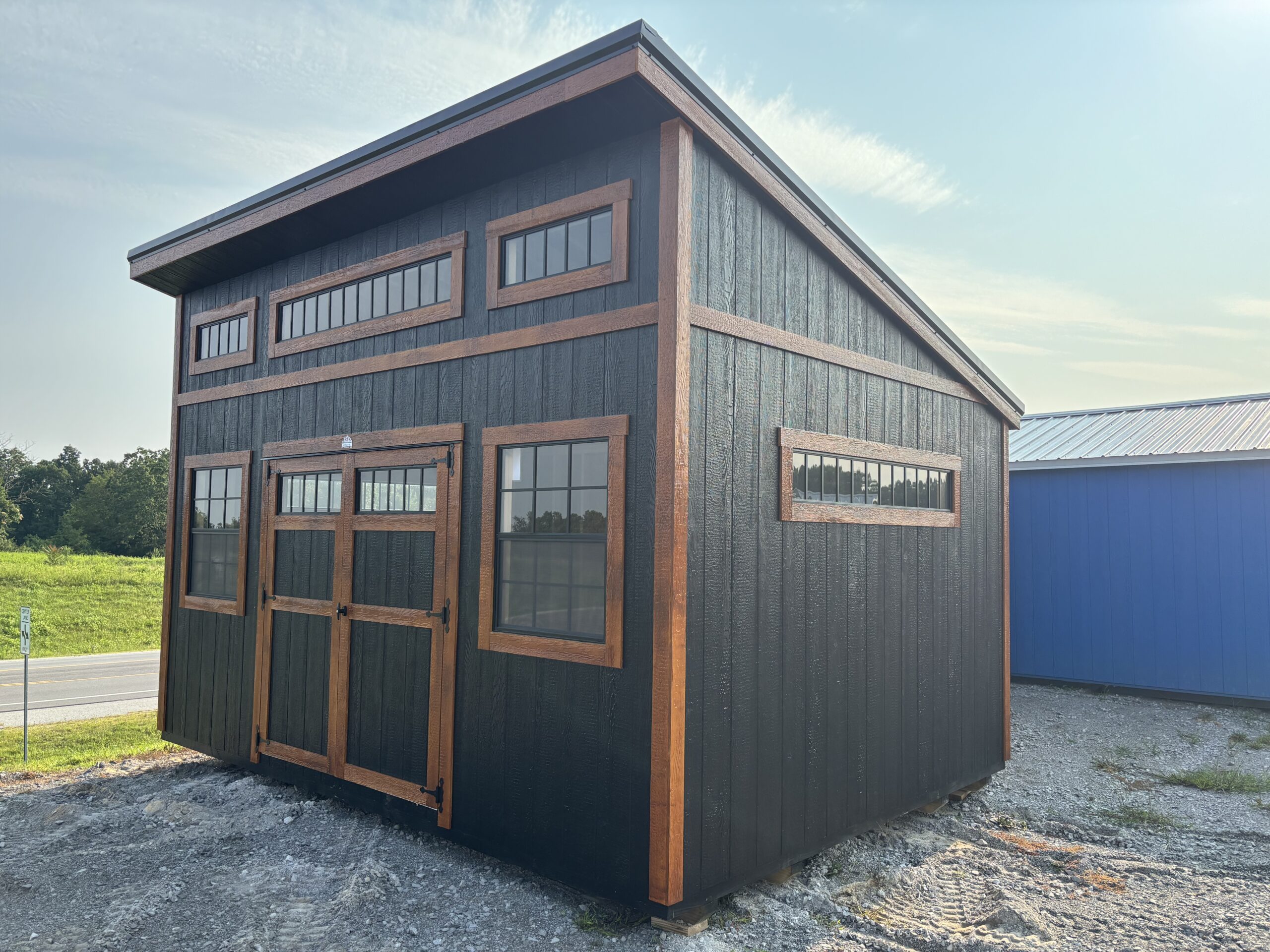 Black barn-style building with brown wooden trim and large rectangular windows on a gravel lot.