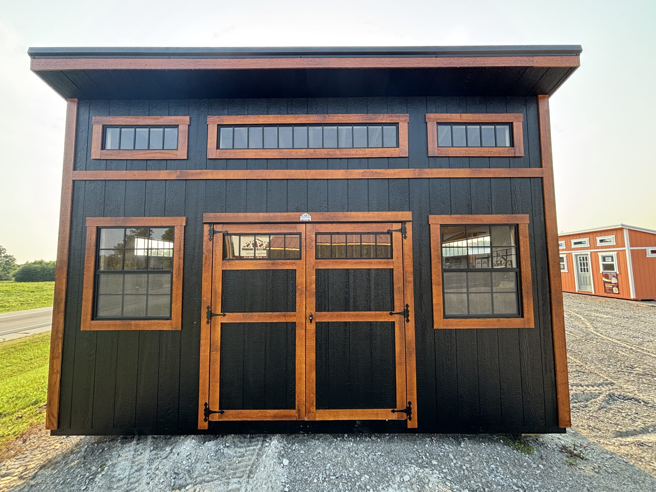 Black exterior shed with natural wood trim, three narrow rectangular windows on the upper level and a large central double door framed in wood.