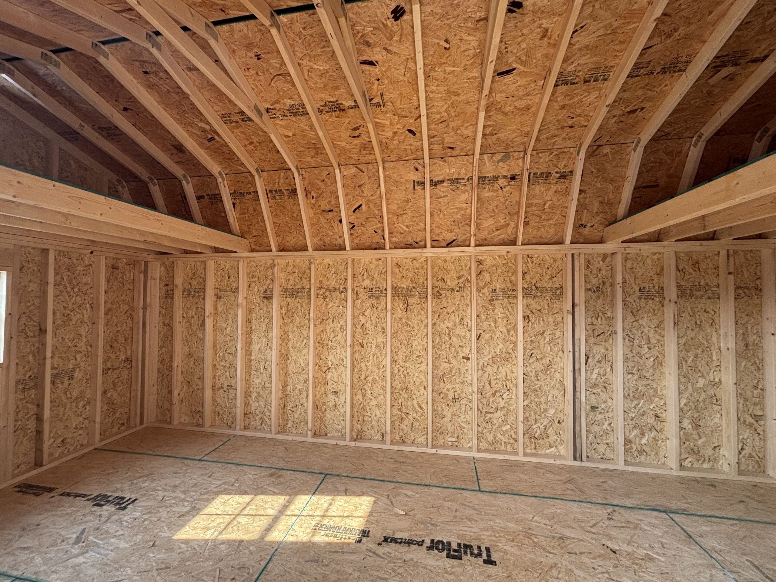 Interior of an unfinished wooden-framed room under construction with exposed studs, OSB walls, and visible roof trusses.