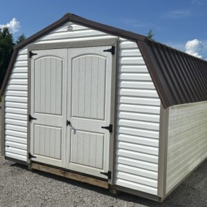 White outdoor storage shed with double arched doors, white siding, and a brown peaked roof on a gravel lot.