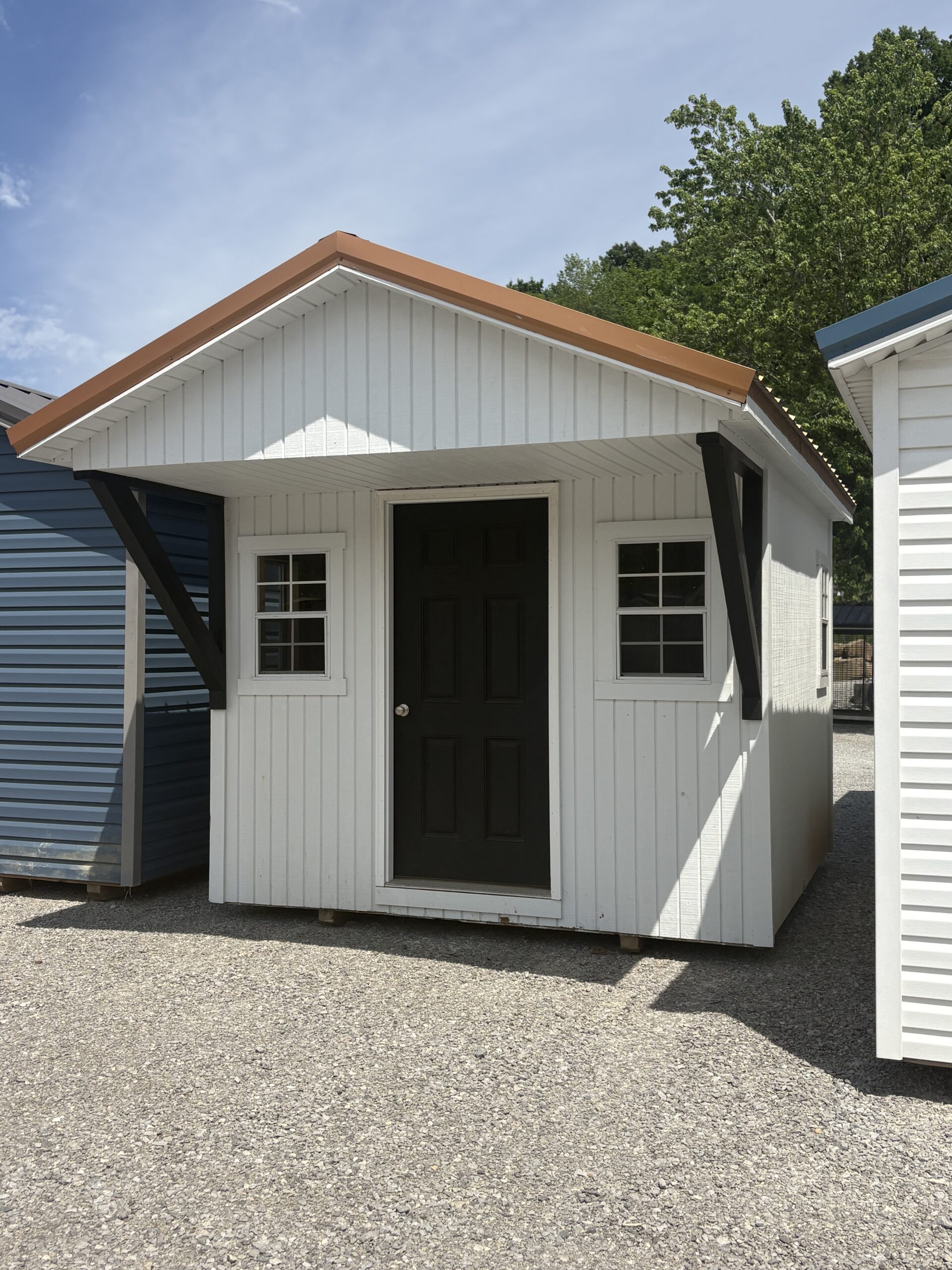 White wooden storage shed with a black front door, two small windows, and orange trim along the gabled roof.