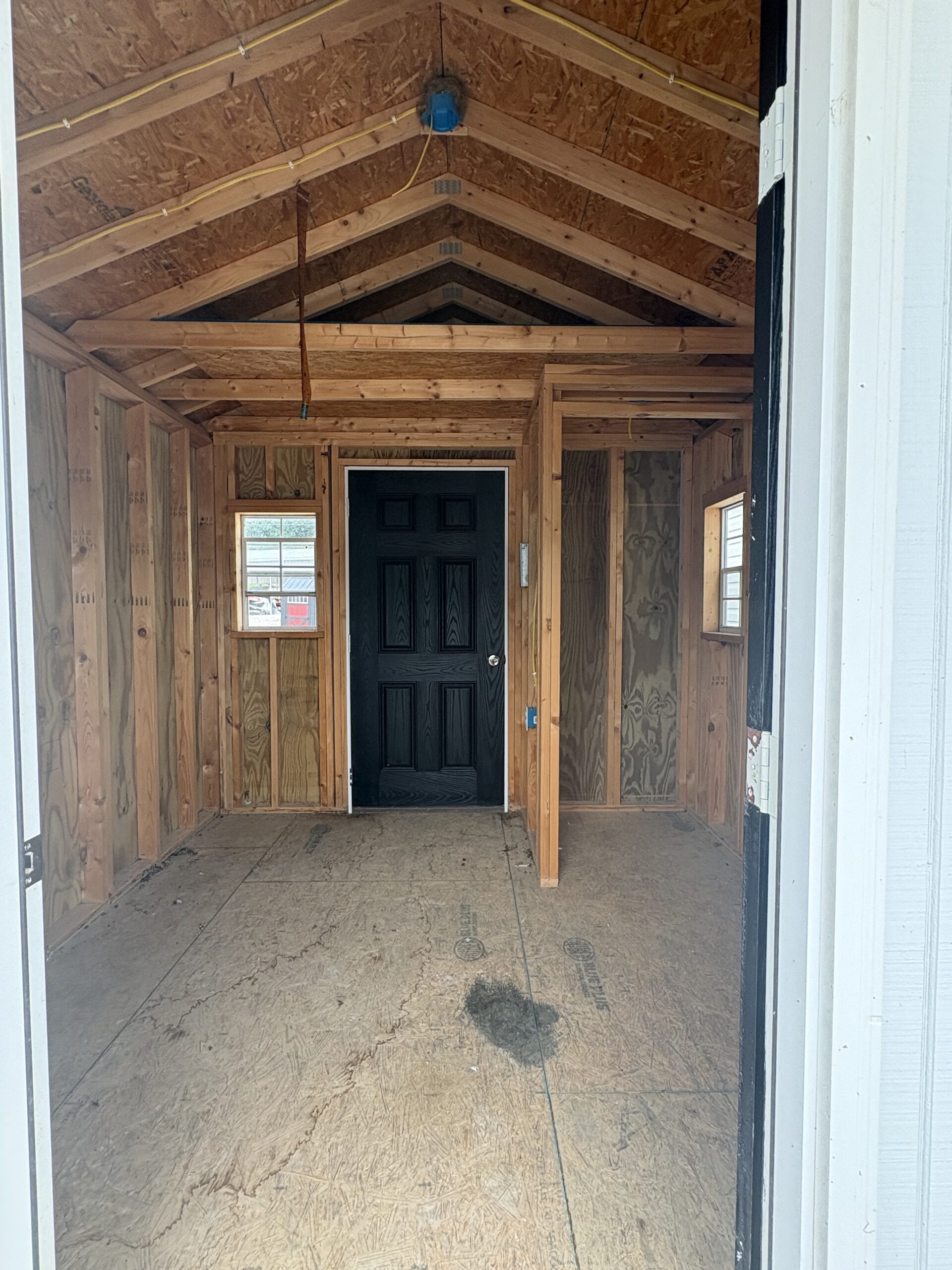 Unfinished entry hall inside a new home; exposed wooden framing, plywood walls, and a dark front door at the far end.