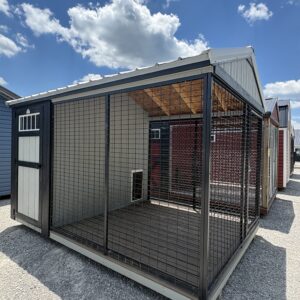 Outdoor metal dog kennel with mesh walls on gravel, featuring a wooden interior and a bright blue sky with clouds behind it