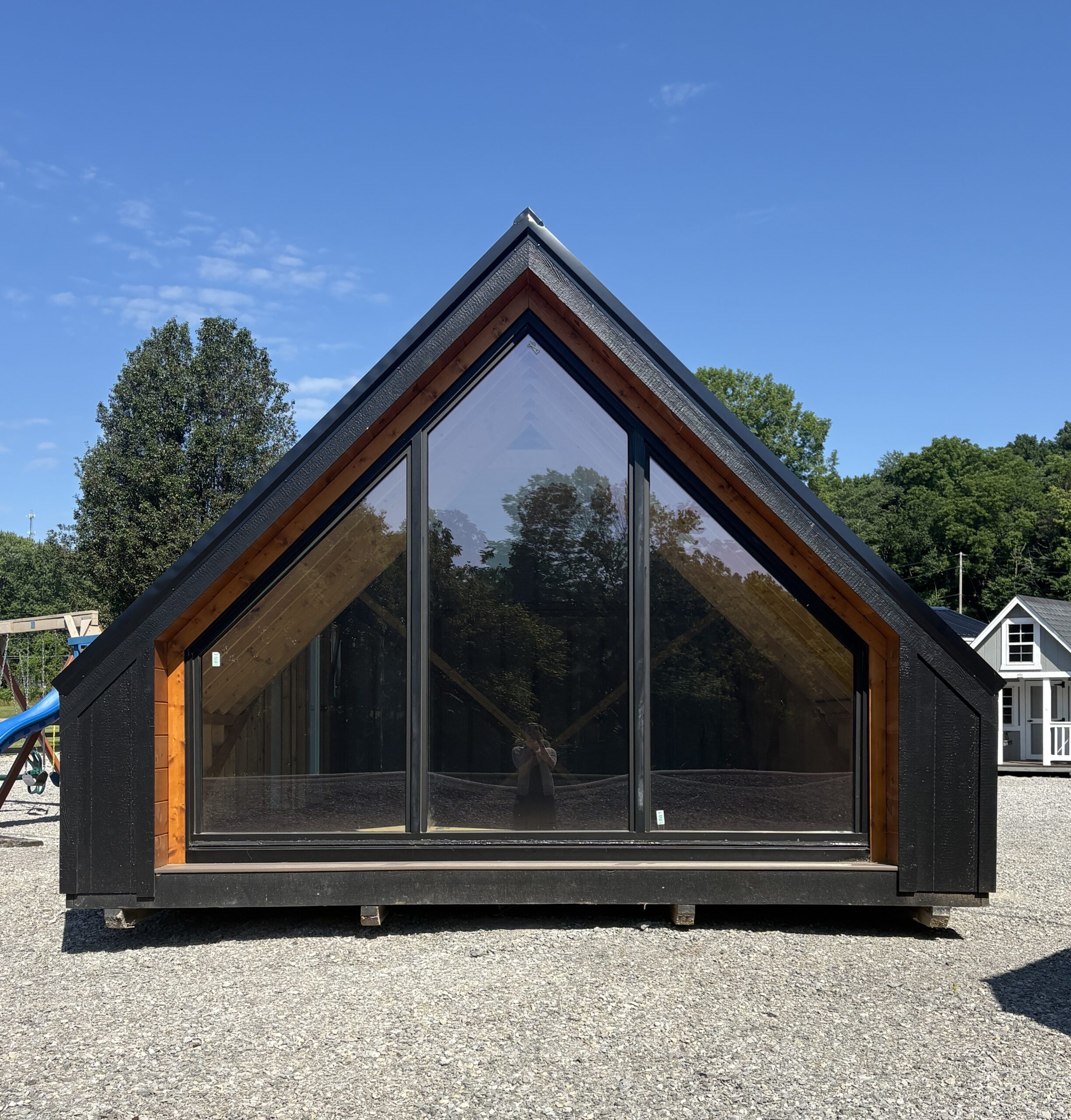 Triangular glass-fronted building with black framing and wooden interior beams under a clear blue sky left of center.