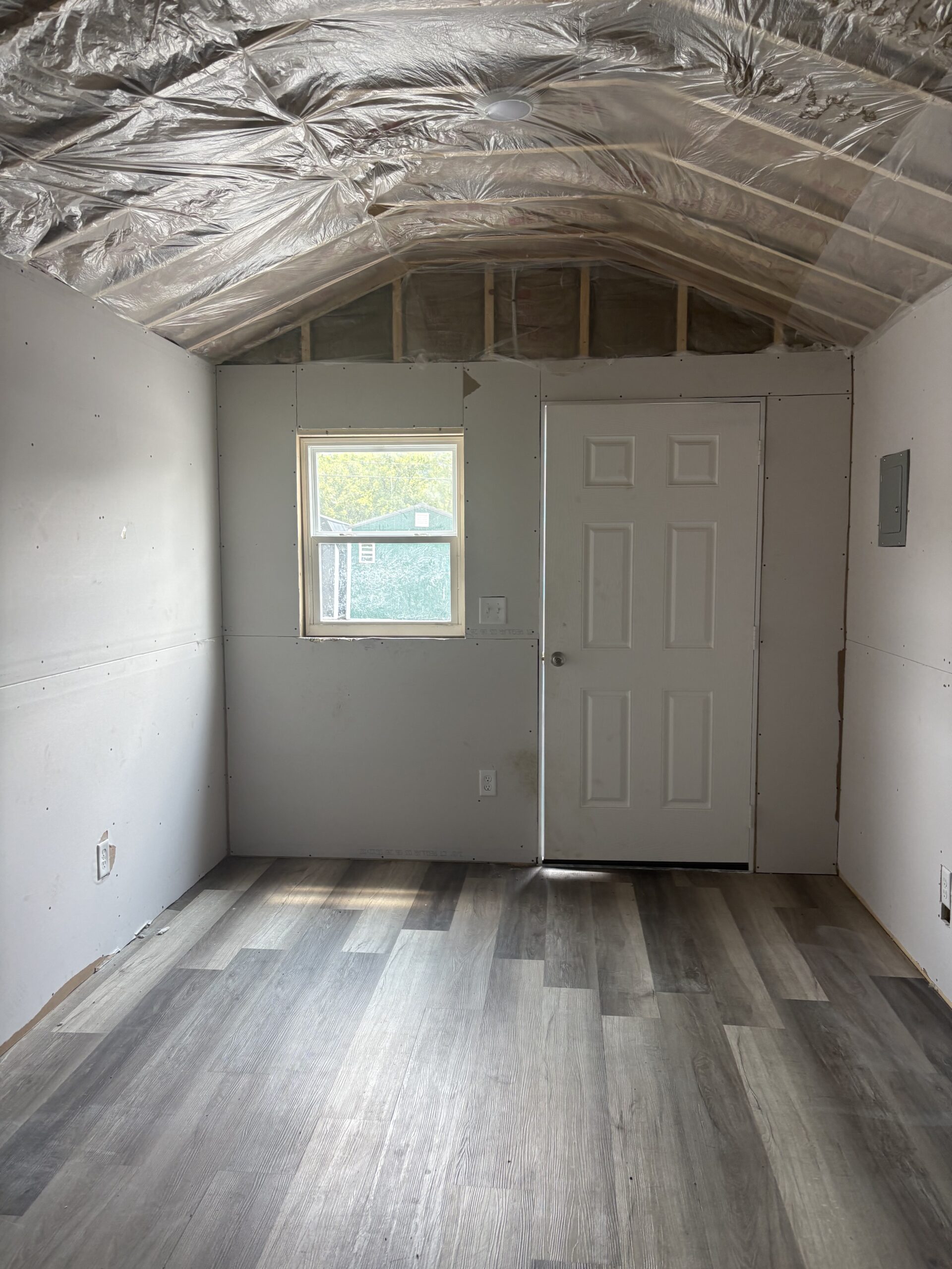 Unfinished renovation room with plastic ceiling cover, partial drywall installed on walls, a white paneled door, and a small window.