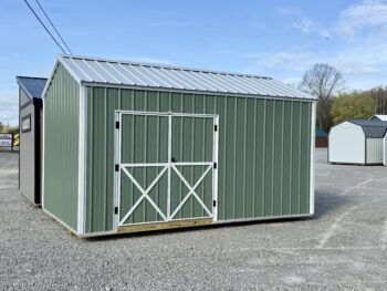 Green metal storage shed with white framing and double barn doors on a gravel lot under a blue sky.