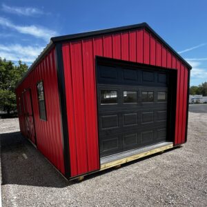 Red metal building with black sectional garage door, set on a gravel lot under a blue sky.