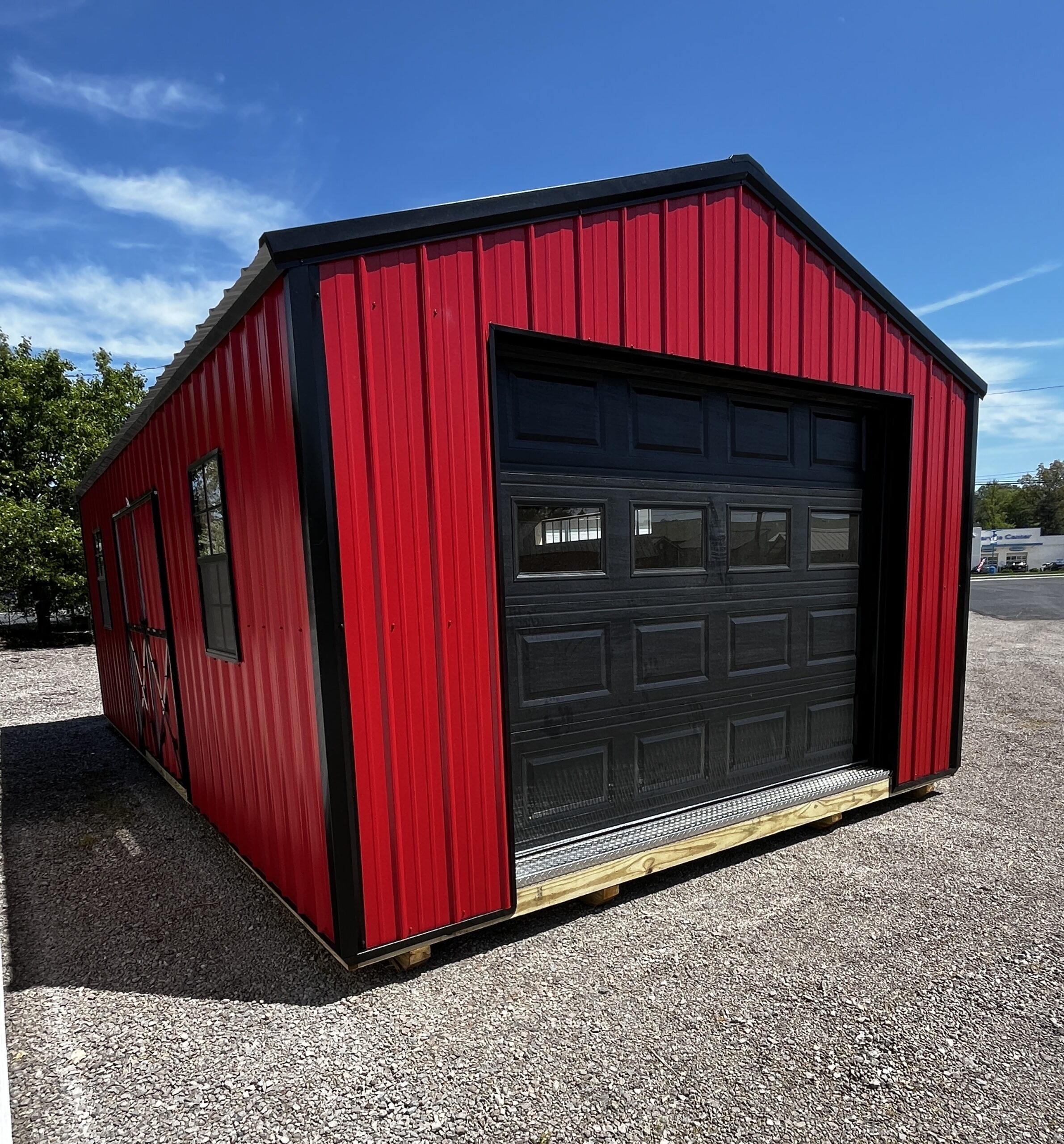 Red metal building with black sectional garage door, set on a gravel lot under a blue sky.