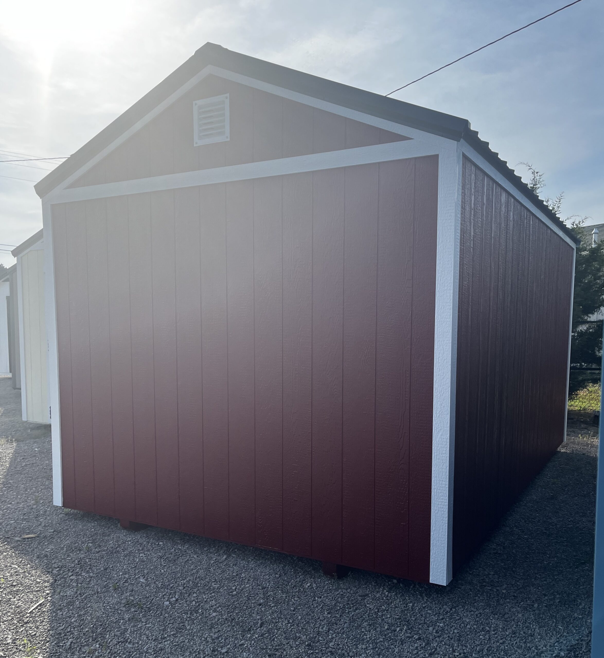 Brown shed with white trim and small vent in the gable, set on gravel. A slanted roof and vertical siding are visible at dusk-like light.