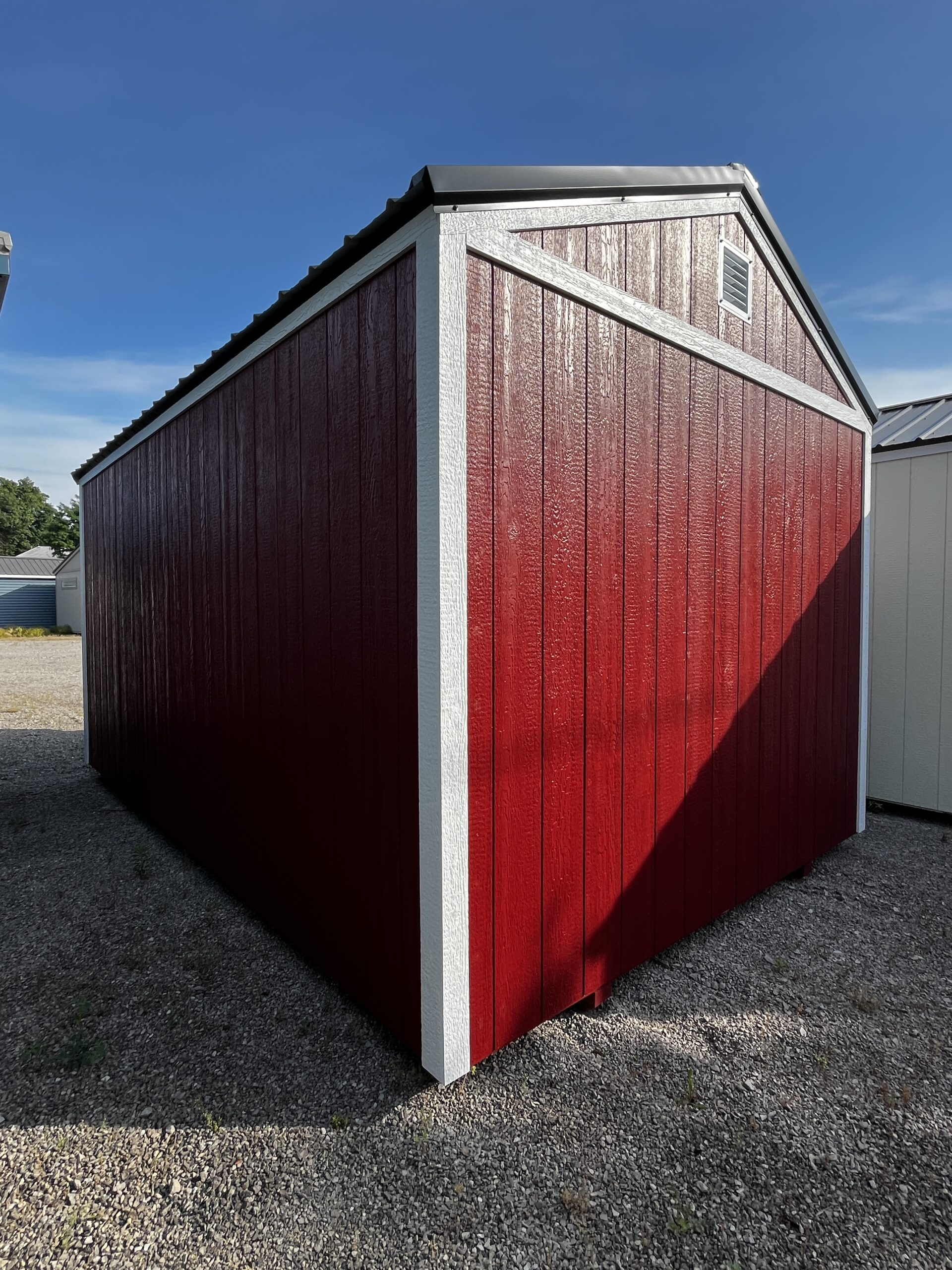 Red wooden shed with white trim and a small vent on the gable, set against a blue sky.