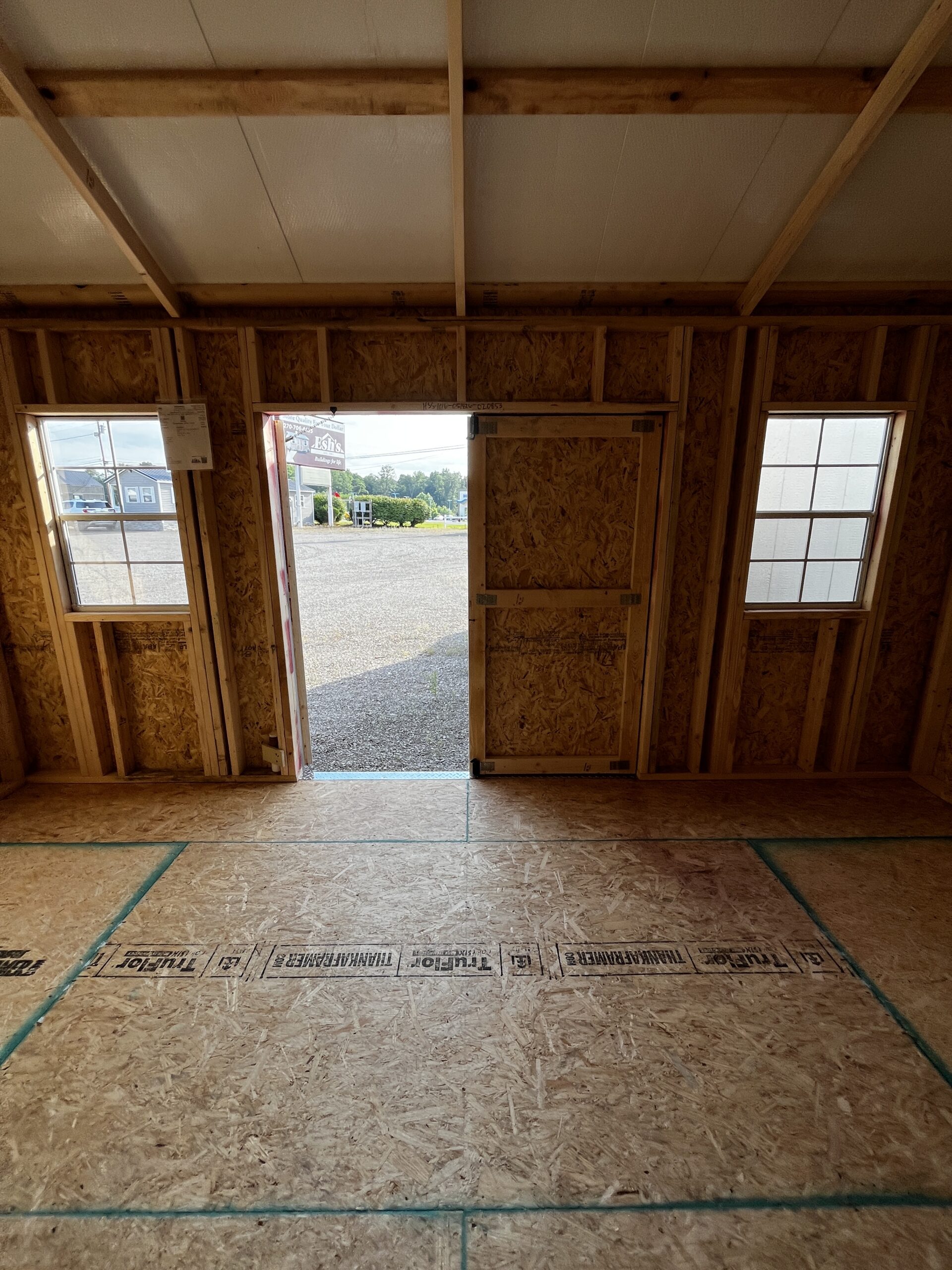 Unfinished room under construction with exposed wooden framing, OSB walls, a doorway to the outdoors, and two windows letting light in.