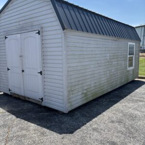 White storage shed with a dark metal sloped roof, double-pane doors, and a side window on an asphalt lot.