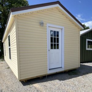 Small beige shed with a white door and a window, raised on blocks on a gravel lot.