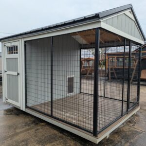 Outdoor animal enclosure attached to a light-gray shed, with black wire mesh walls and a wooden floor.