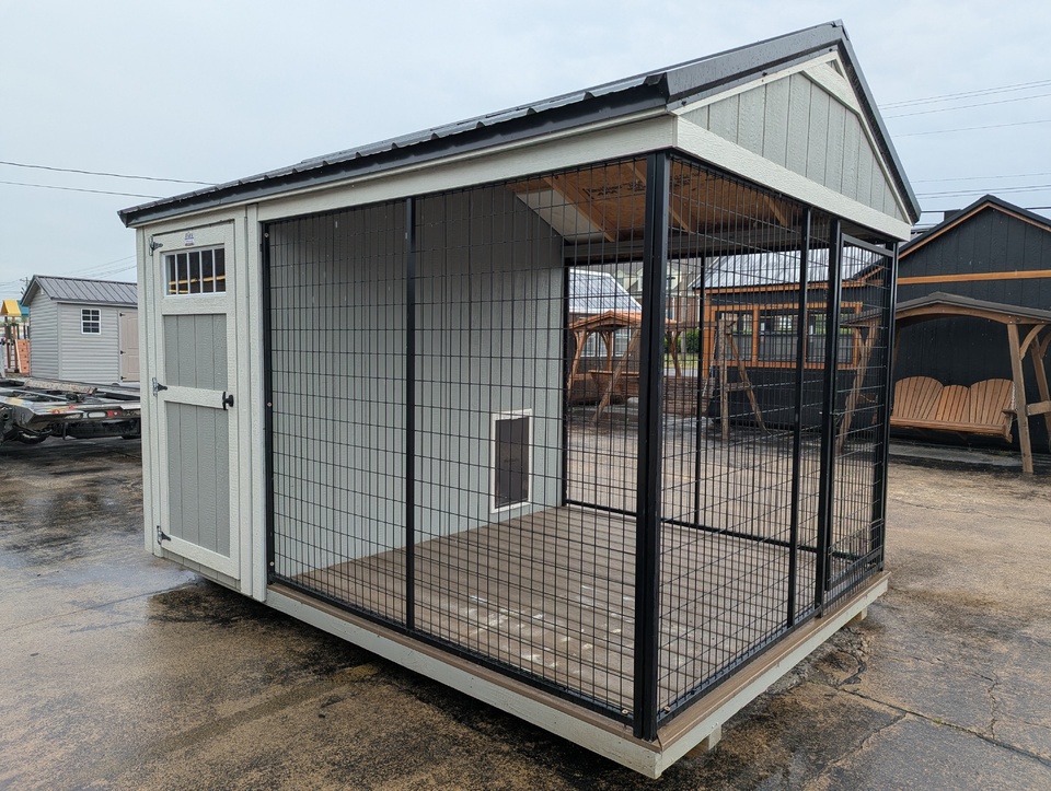 Outdoor animal enclosure attached to a light-gray shed, with black wire mesh walls and a wooden floor.