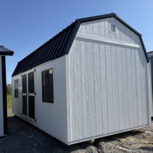 White shed with a dark gabled roof, double doors with glass panes, and a side window on a gravel surface under a clear blue sky.
