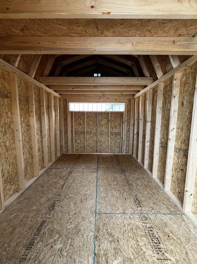 Interior of an unfinished wooden shed with exposed framing, OSB walls, and a peaked ceiling
